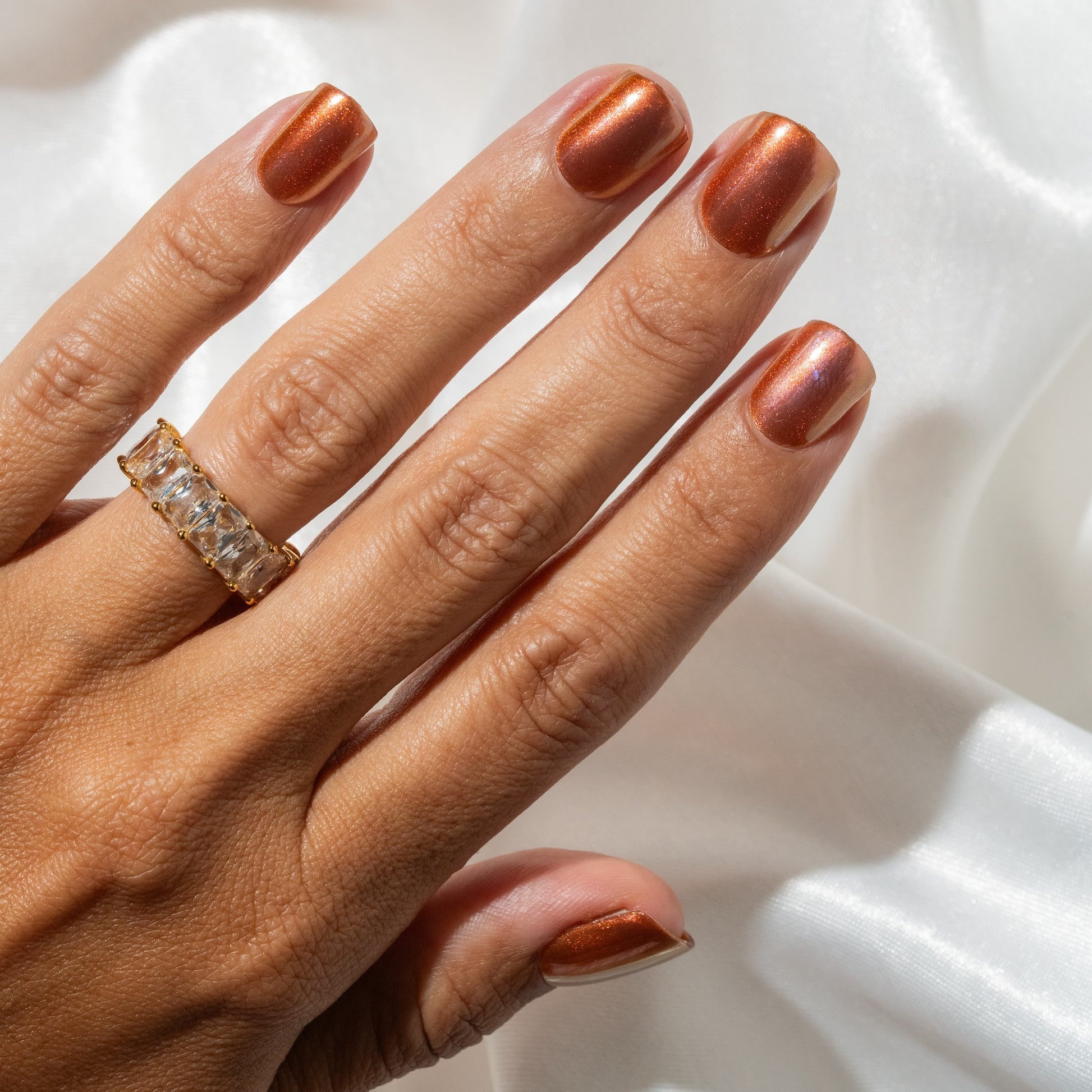 Hand with metallic press on nails and a ring on a white background