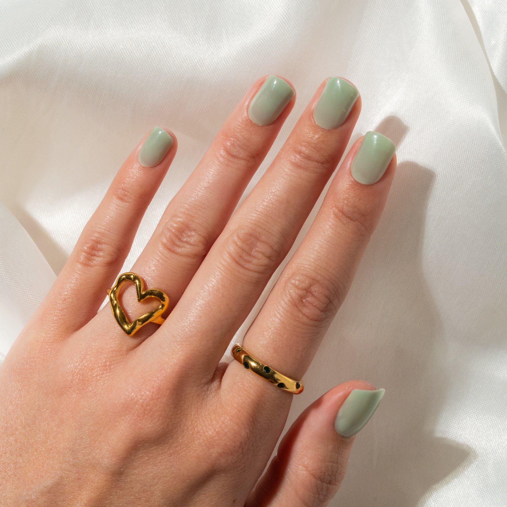 Hand with gold heart-shaped ring and light green press on nails on a white background