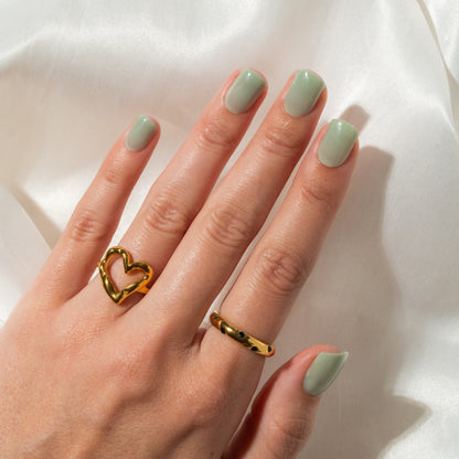 Hand with gold heart-shaped ring and light green press on nails on a white background