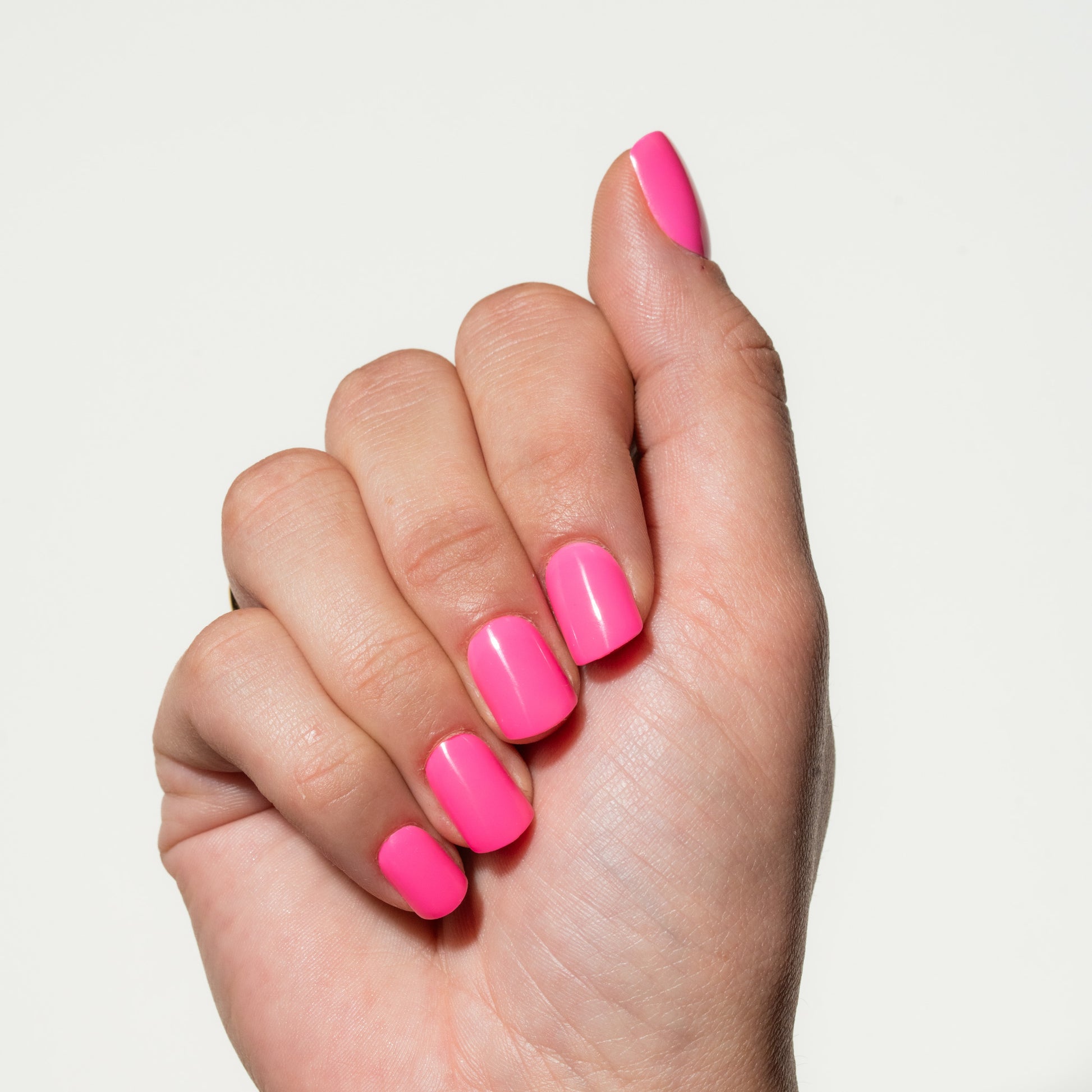 Hand with neon pink press on nails on a light gray background