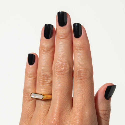 Hand with black press on nails wearing a gold ring on a light background
