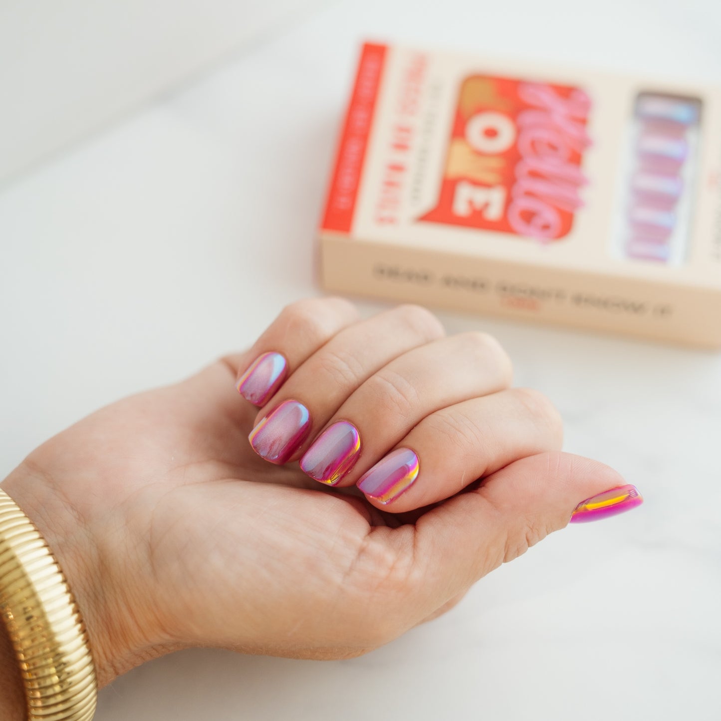 Hand with shiny pink press on nails, with a box in the background