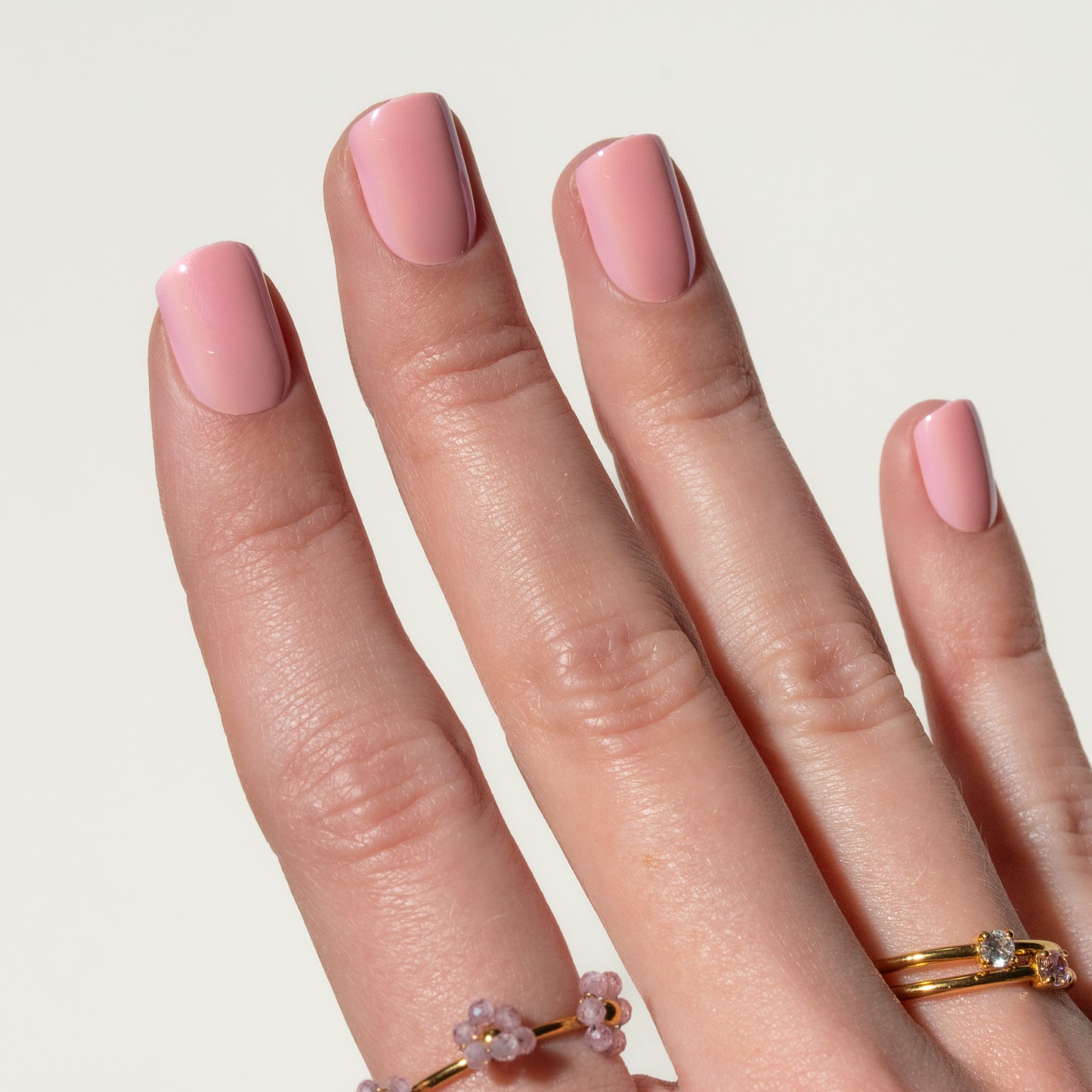 Close-up of a hand with pink press on nails and gold rings on a light background