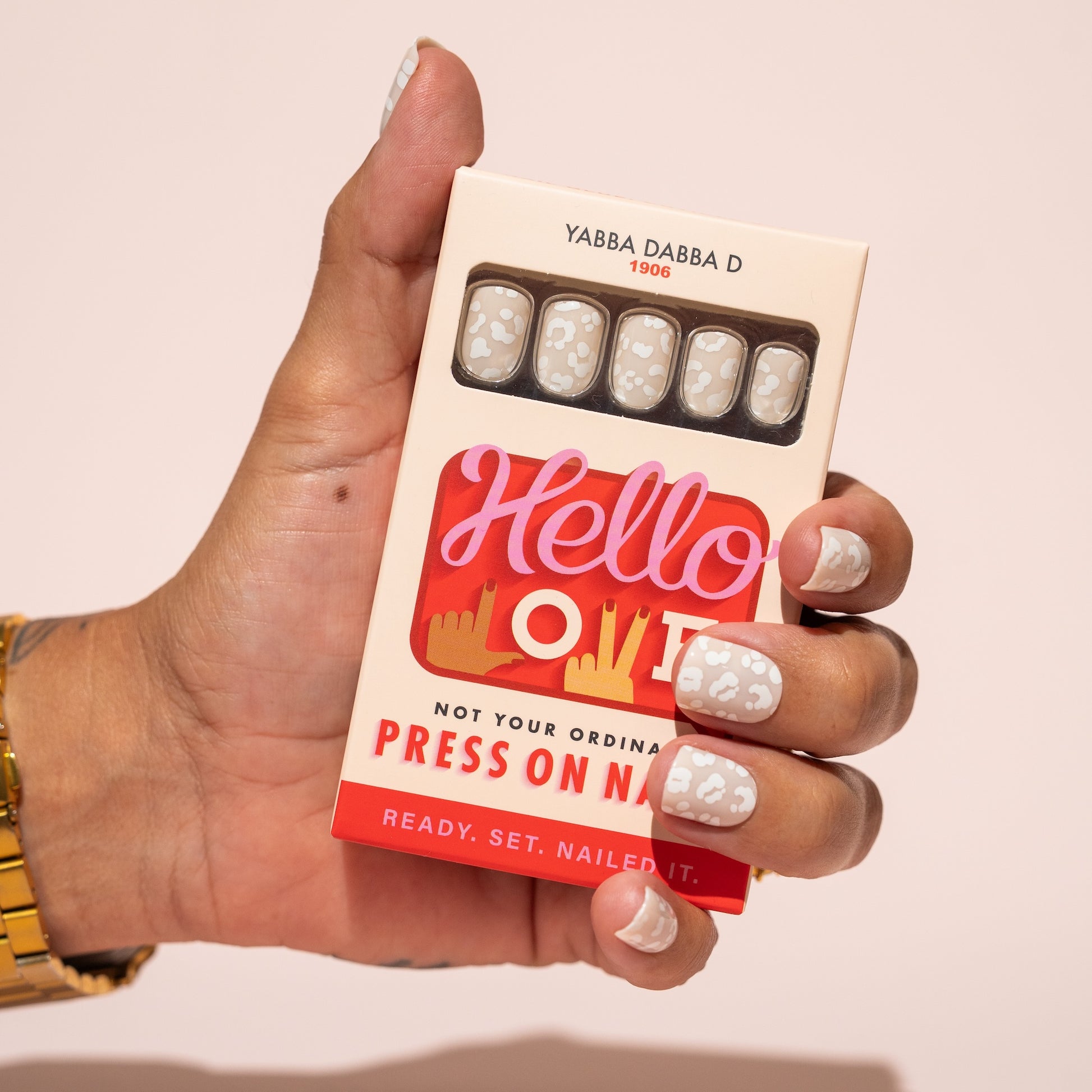 Hand holding a box of Hello Love press on nails with a pink background