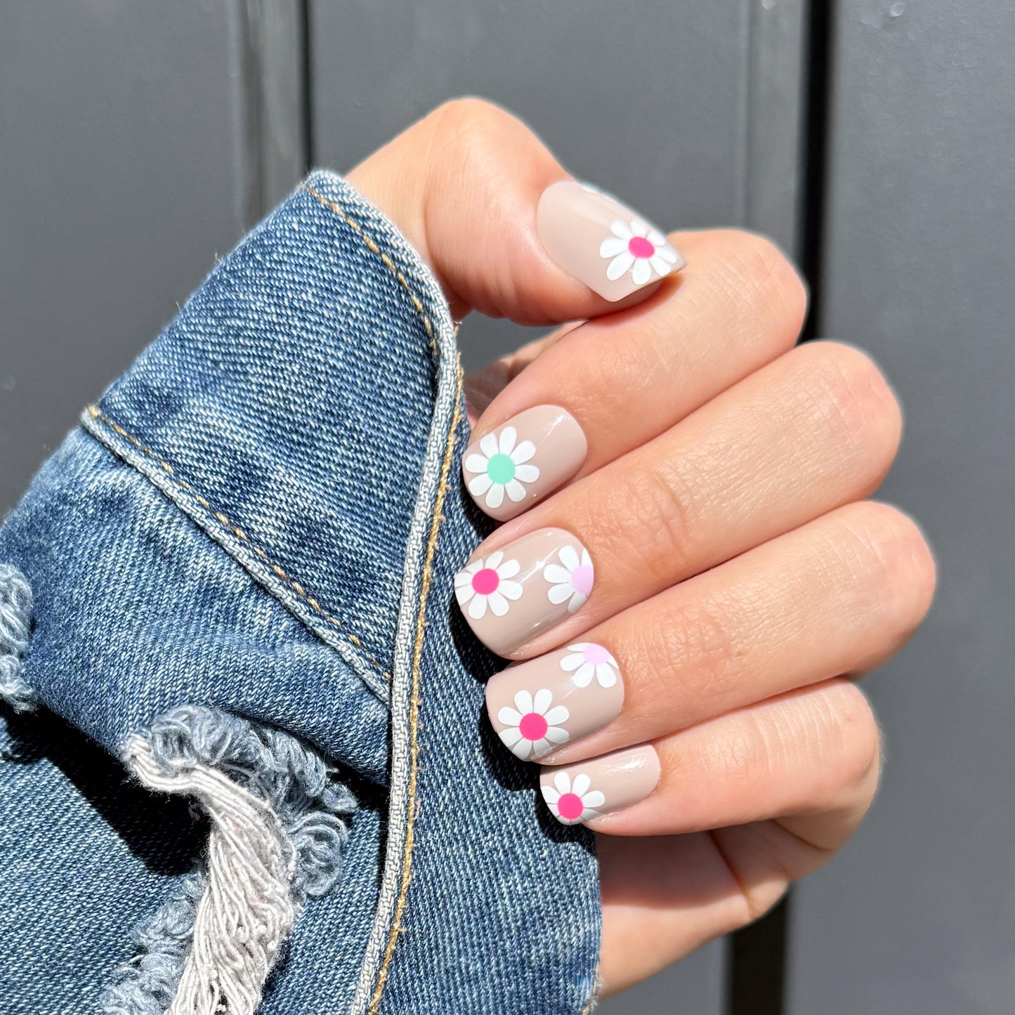 Hand with floral nail design wearing a denim jacket against a gray background