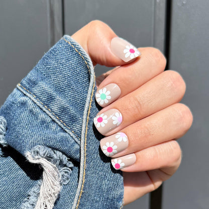 Hand with floral nail design wearing a denim jacket against a gray background