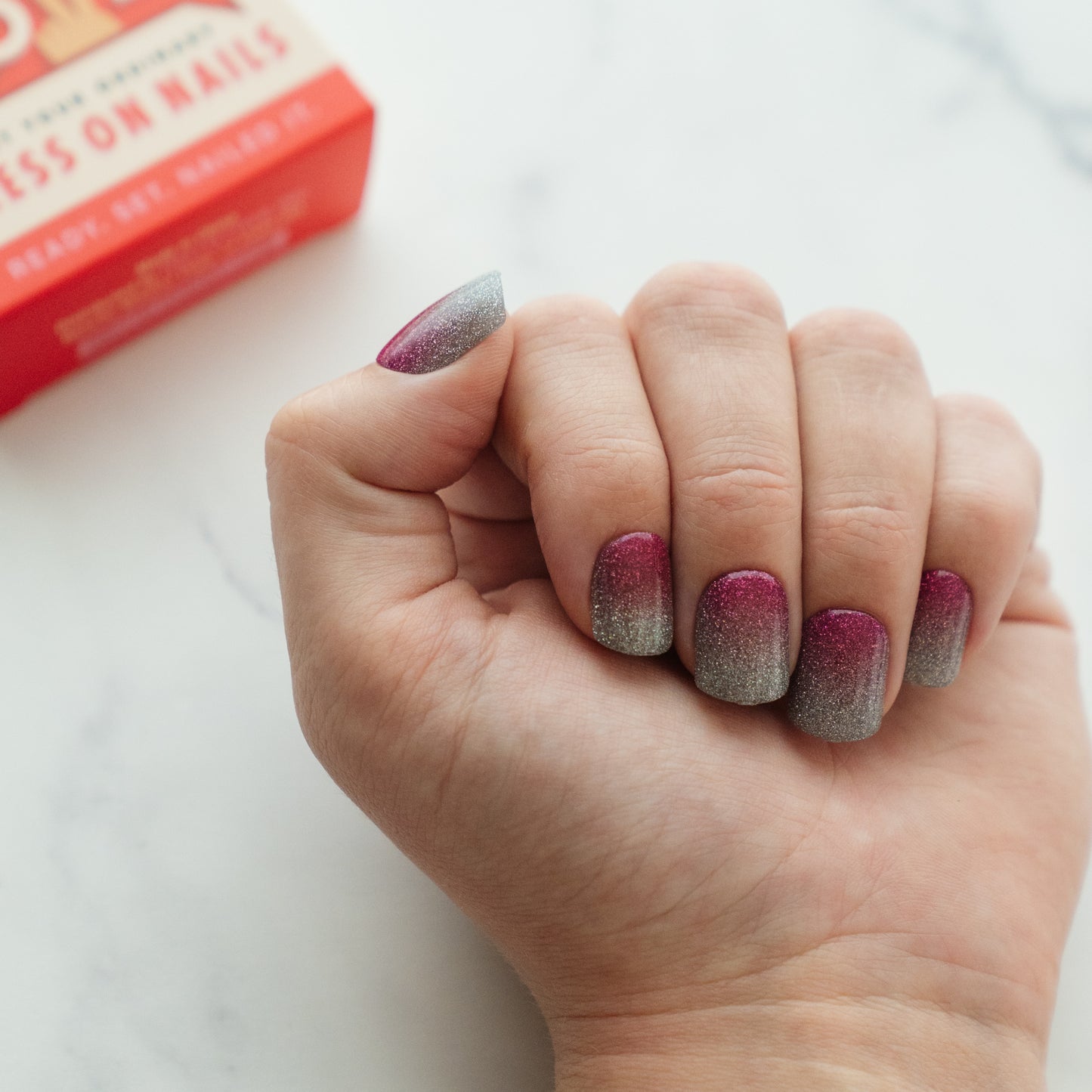 Hand with ombre press on nails holding a box of nail products