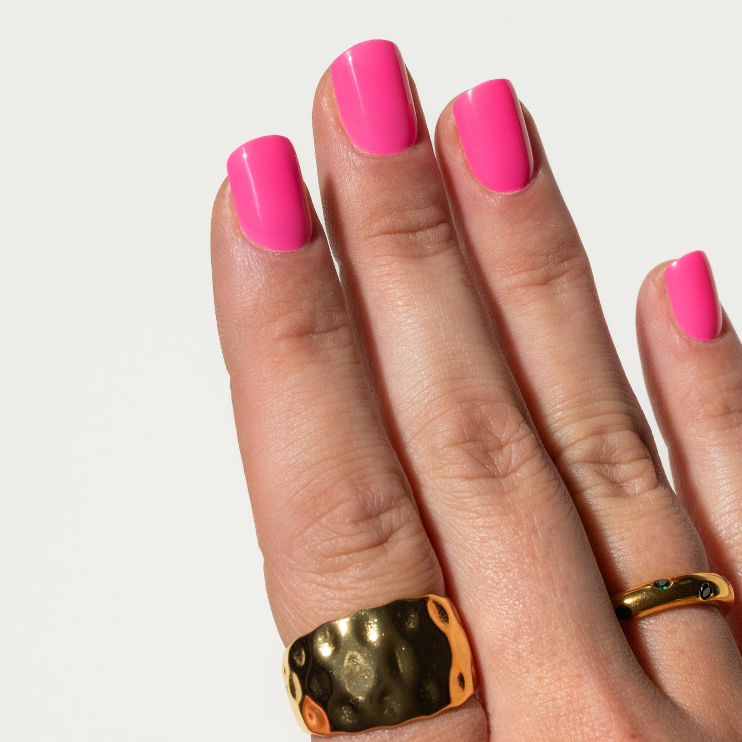 Hand with pink press on nails and gold rings on a white background