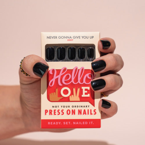 Hand holding a box of press-on nails with Hello Love on a pink background