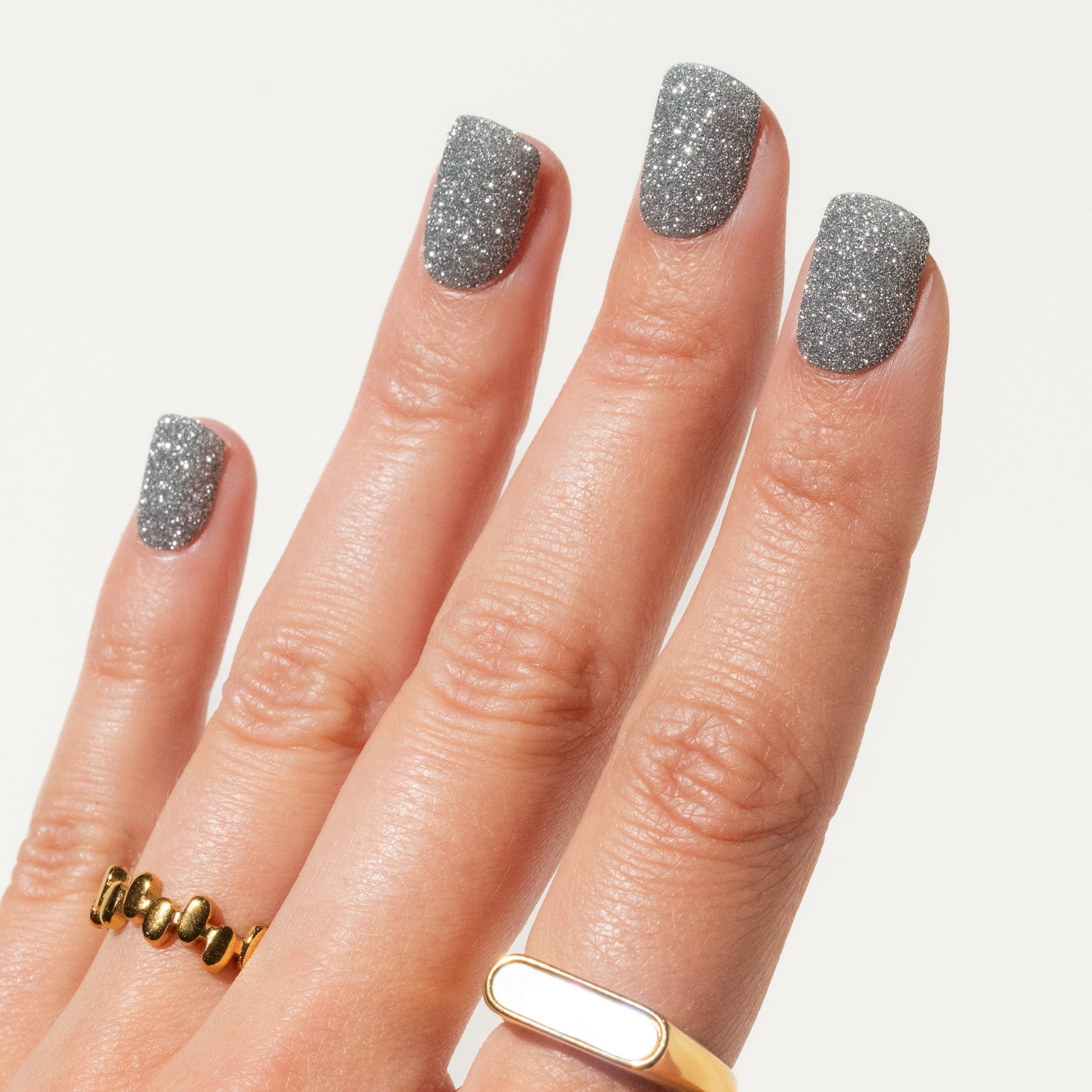 Close-up of a hand with glittery silver press on nails  on a light background