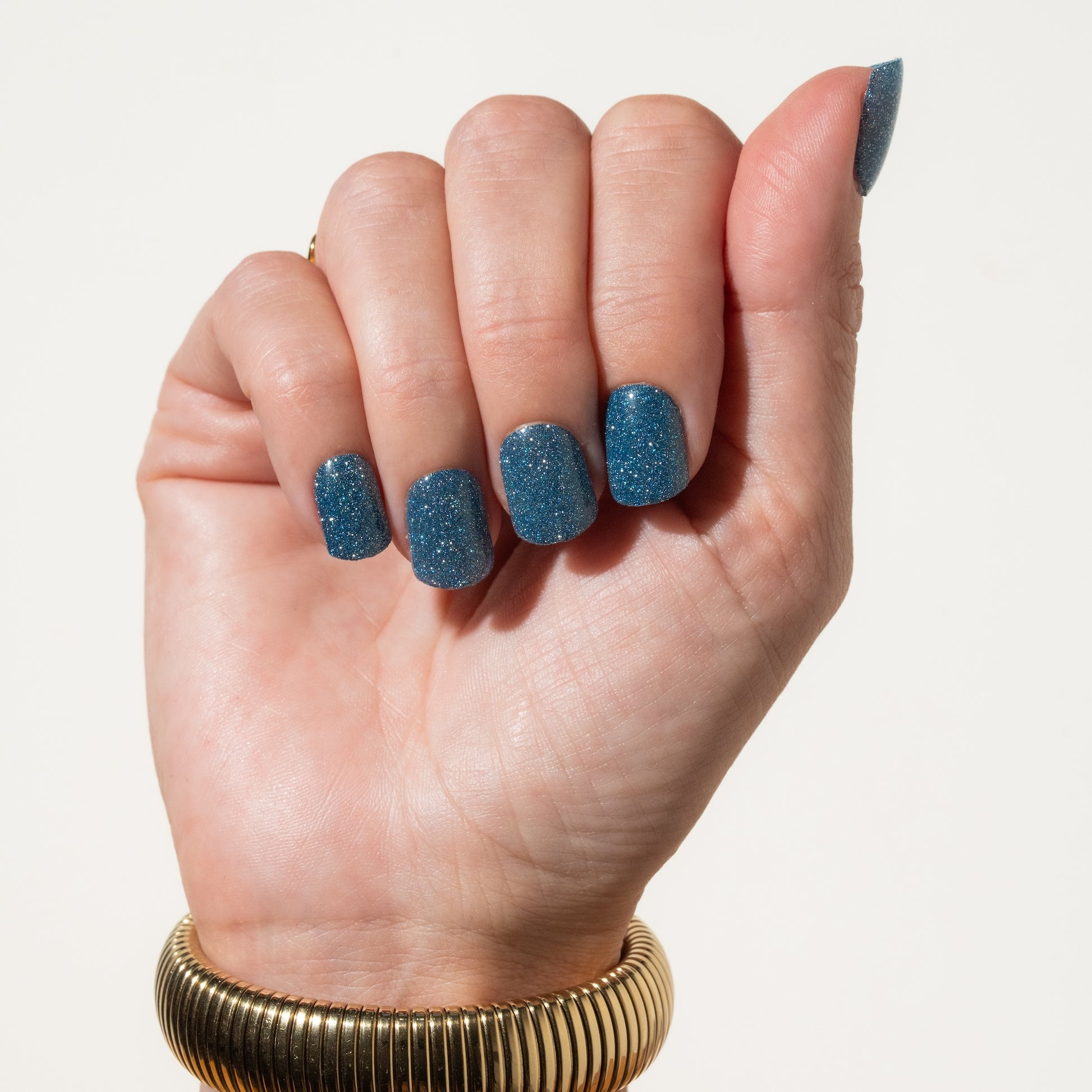 Hand with blue glittery blue press on nails on a plain background