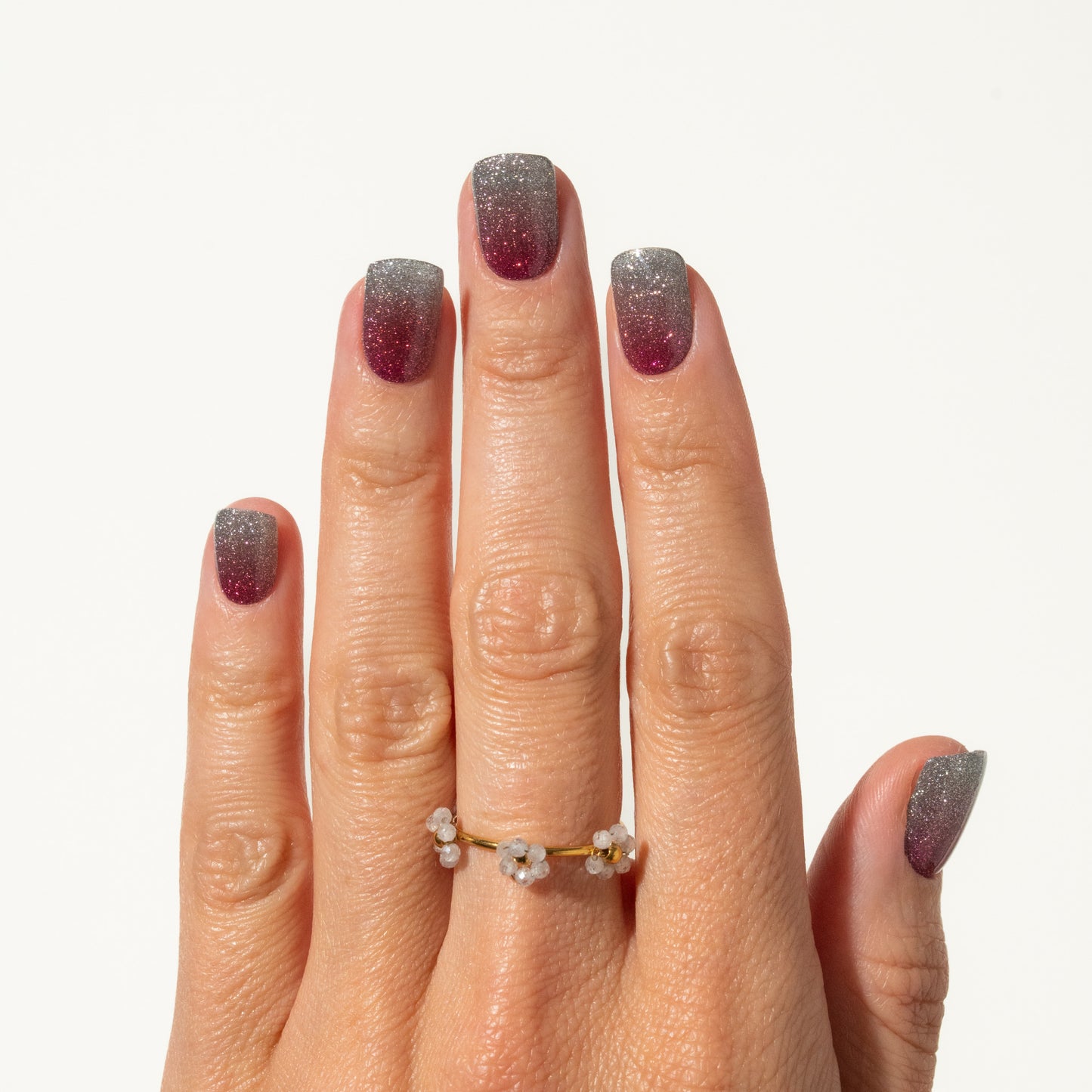 Hand with glittery nails wearing a gold ring on a white background