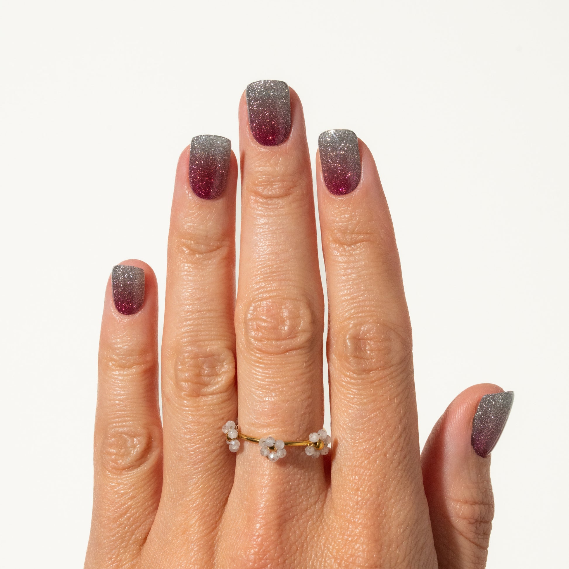 Hand with glittery nails wearing a gold ring on a white background