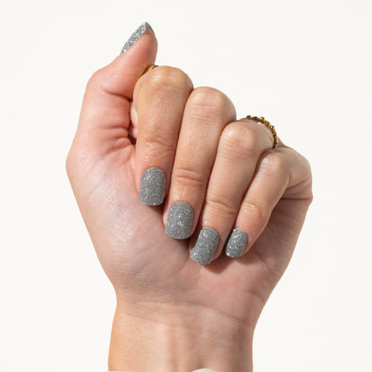 Hand with glittery silver press on nails on a white background