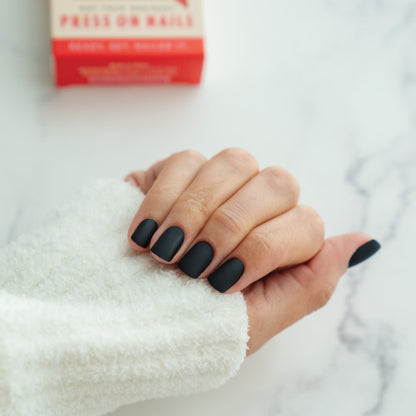 Hand with black press on nails holding a with a red box in the background.