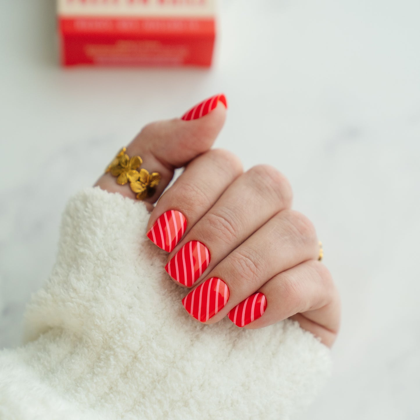 Hand with red striped press on nails wearing a gold ring on a white background