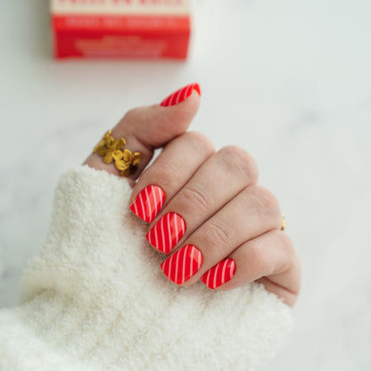 Hand with red striped press on nails wearing a gold ring on a white background