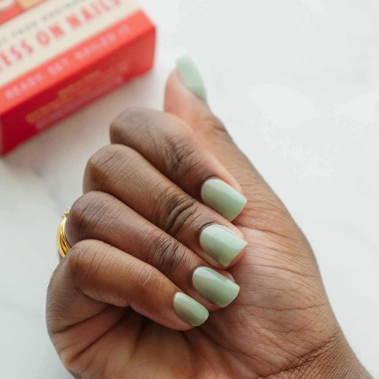 Hand with light green nail polish holding a red box on a white background