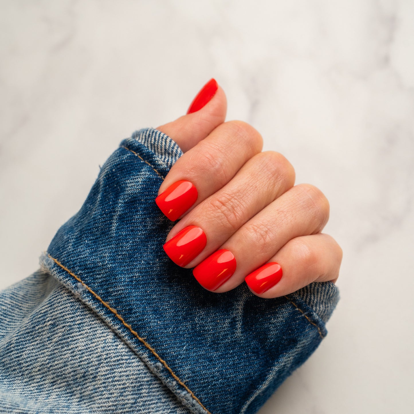 Hand with red press on nails wearing a denim sleeve on a light background