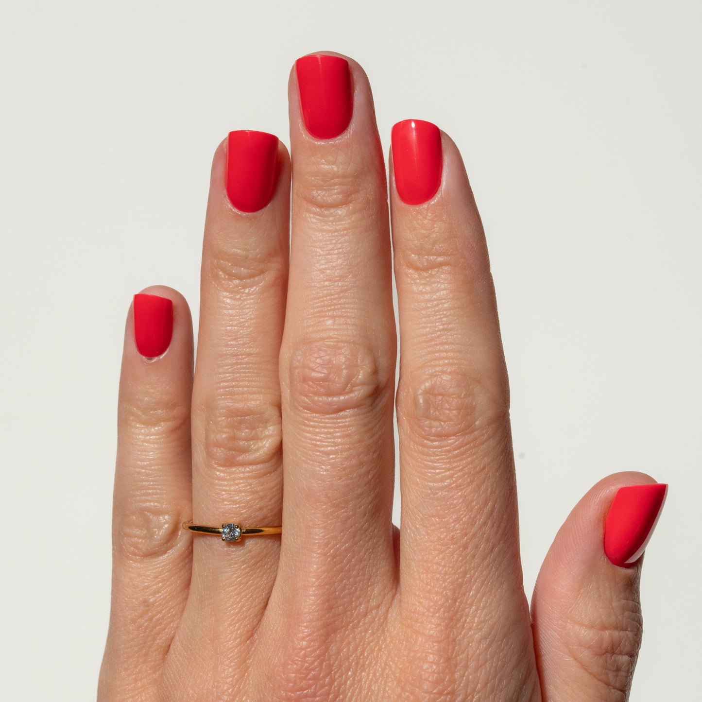 Hand with red press on nails wearing a gold ring on a light gray background