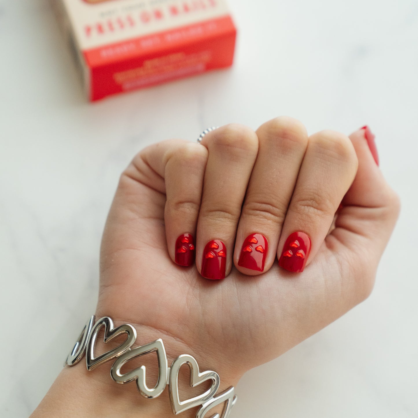 Hand with valentine's day press on nails and silver heart bracelet on a white background