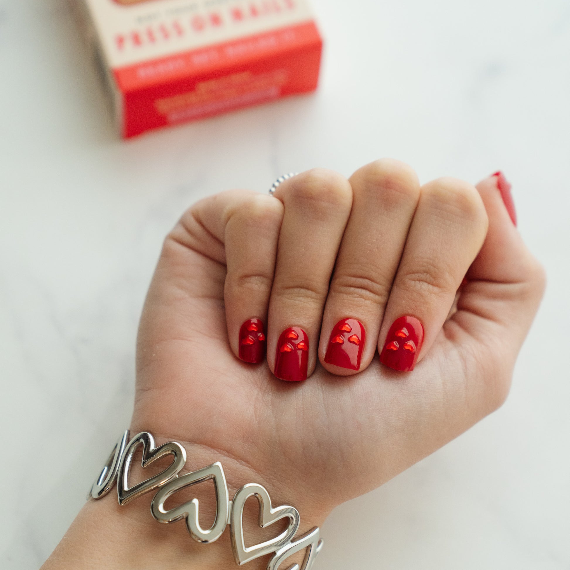Hand with valentine's day press on nails and silver heart bracelet on a white background