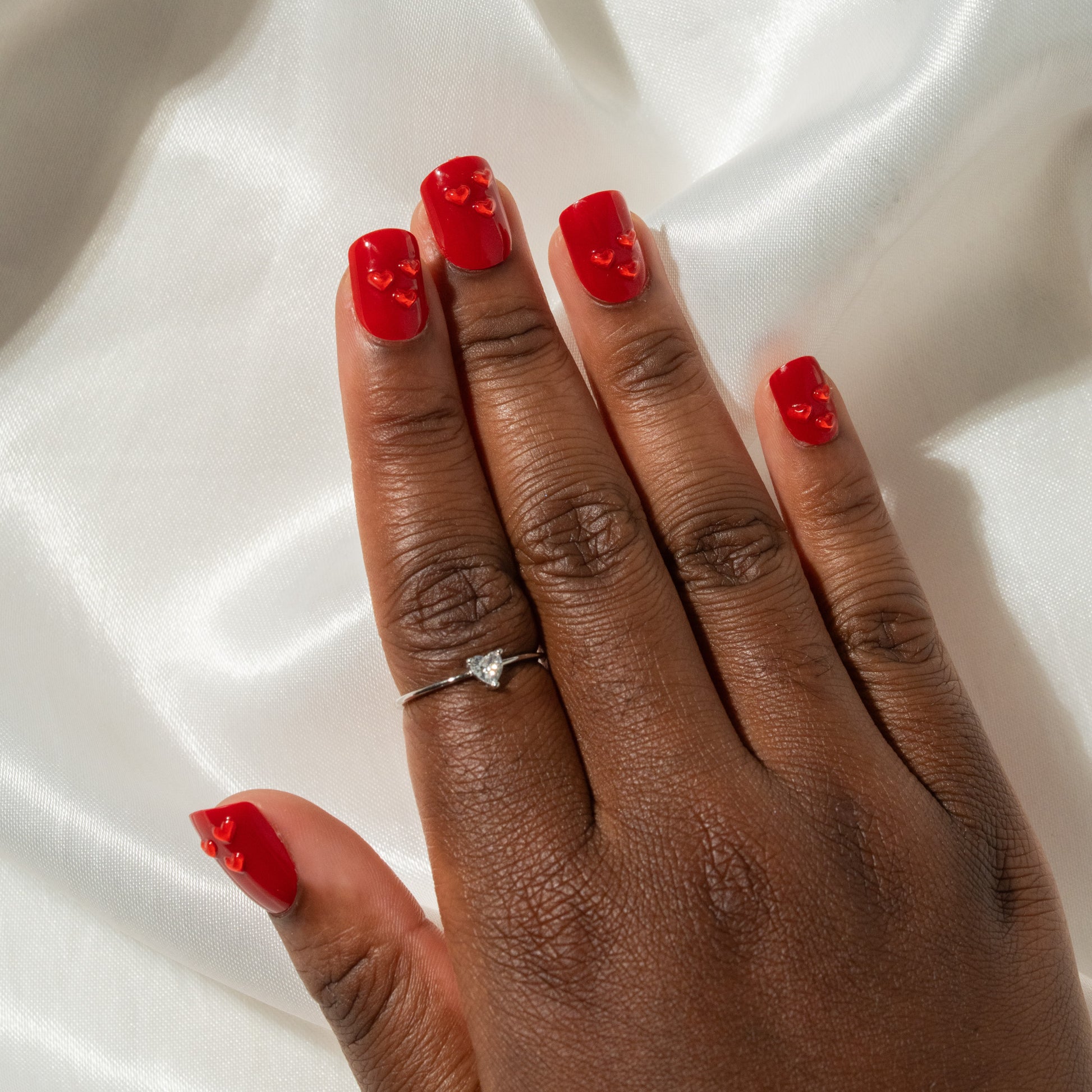Hand with red press on nails a white fabric background