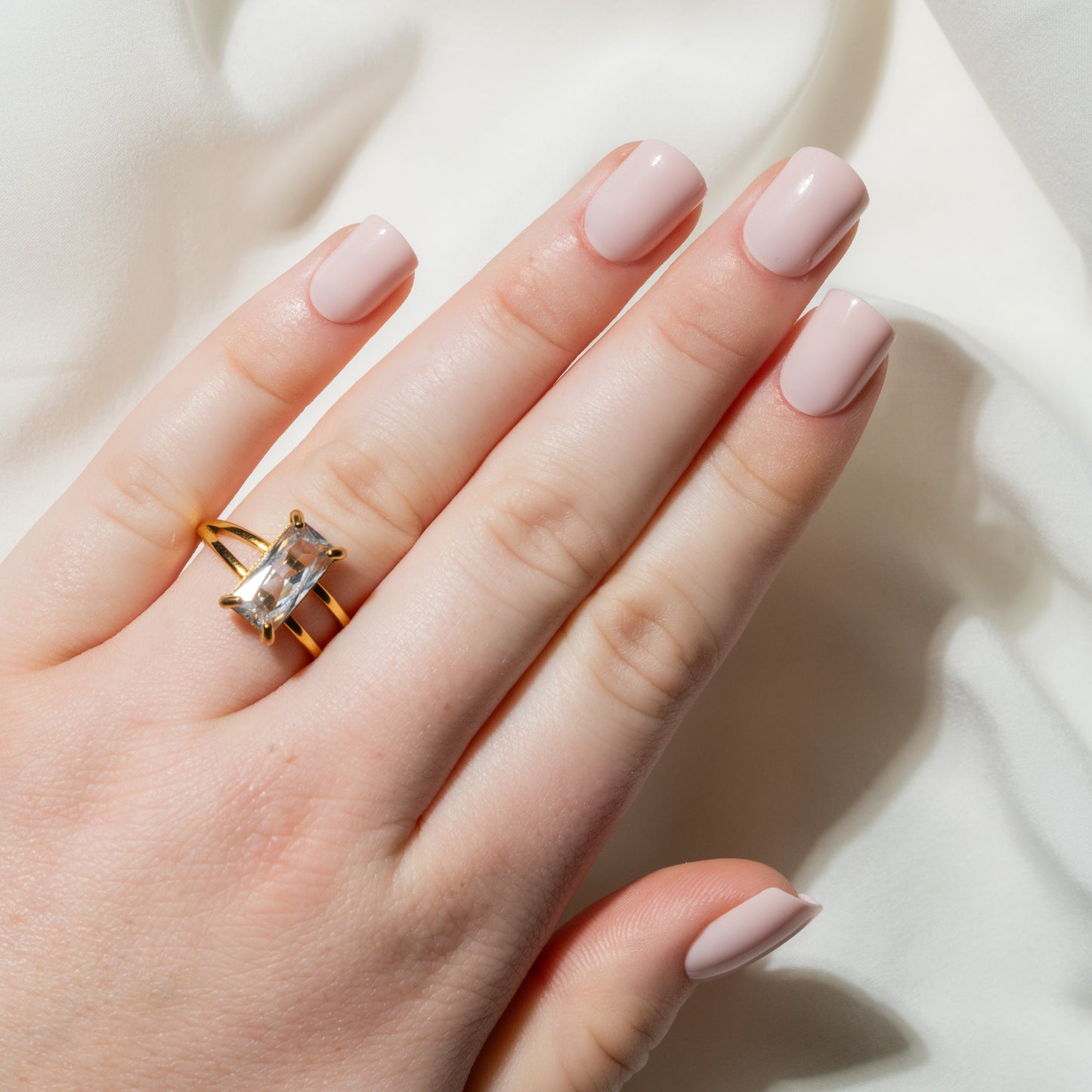 Hand with pink press on nails wearing a gold ring on a light background