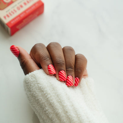 Hand with red and pink striped nail press on nails on a white background