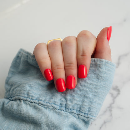 Hand with red nail polish wearing a gold ring, against a light blue denim background.