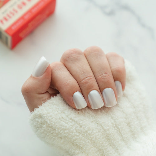 Hand with white press on nails holding a fluffy white object on a light background