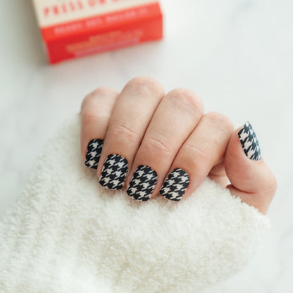 Hand with houndstooth patterned press on nails on a white background